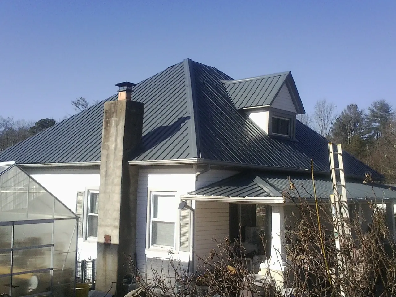 Dark blue standing seam metal roof on a white farmhouse with dormer — Slate & Tile Roof Repair by Roofing Brothers in Glade Park