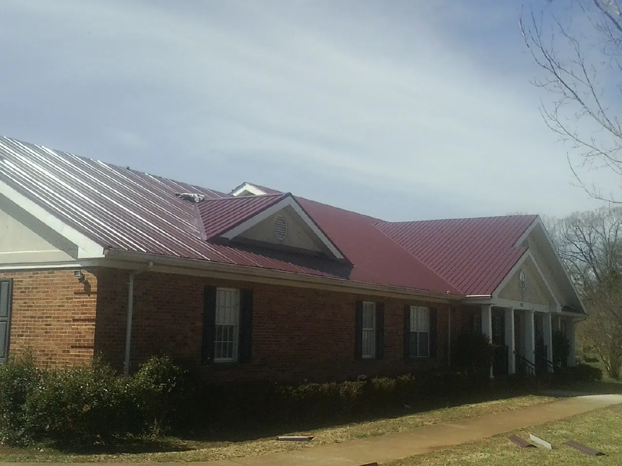 Red metal roof with gabled entries on a long brick building, from a Hail Damage Roof Repair job in Glade Park
