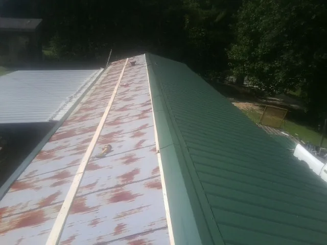 Old rusted panels beside newly installed green metal roofing — Wind Damage Roof Repair by Roofing Brothers in Glade Park