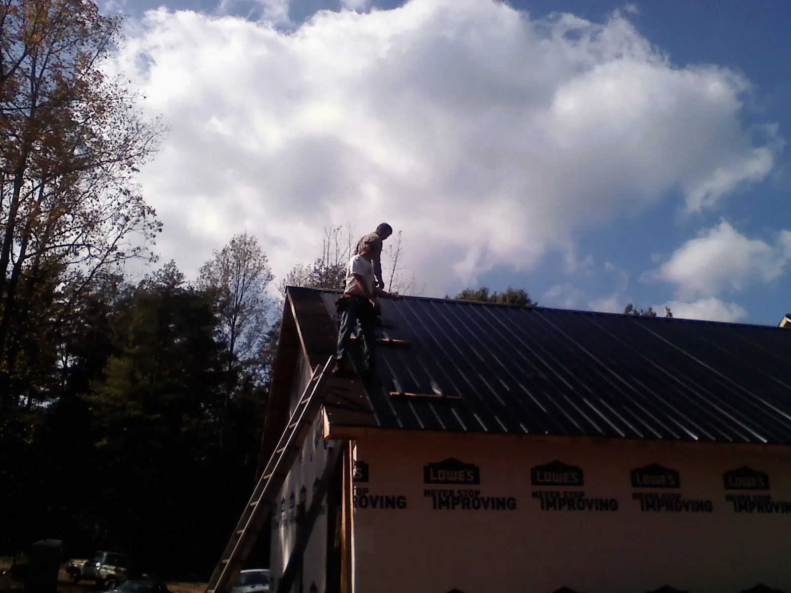 Roofer fastening dark metal panels high against a cloudy sky, from a Roof Inspection job in Glade Park