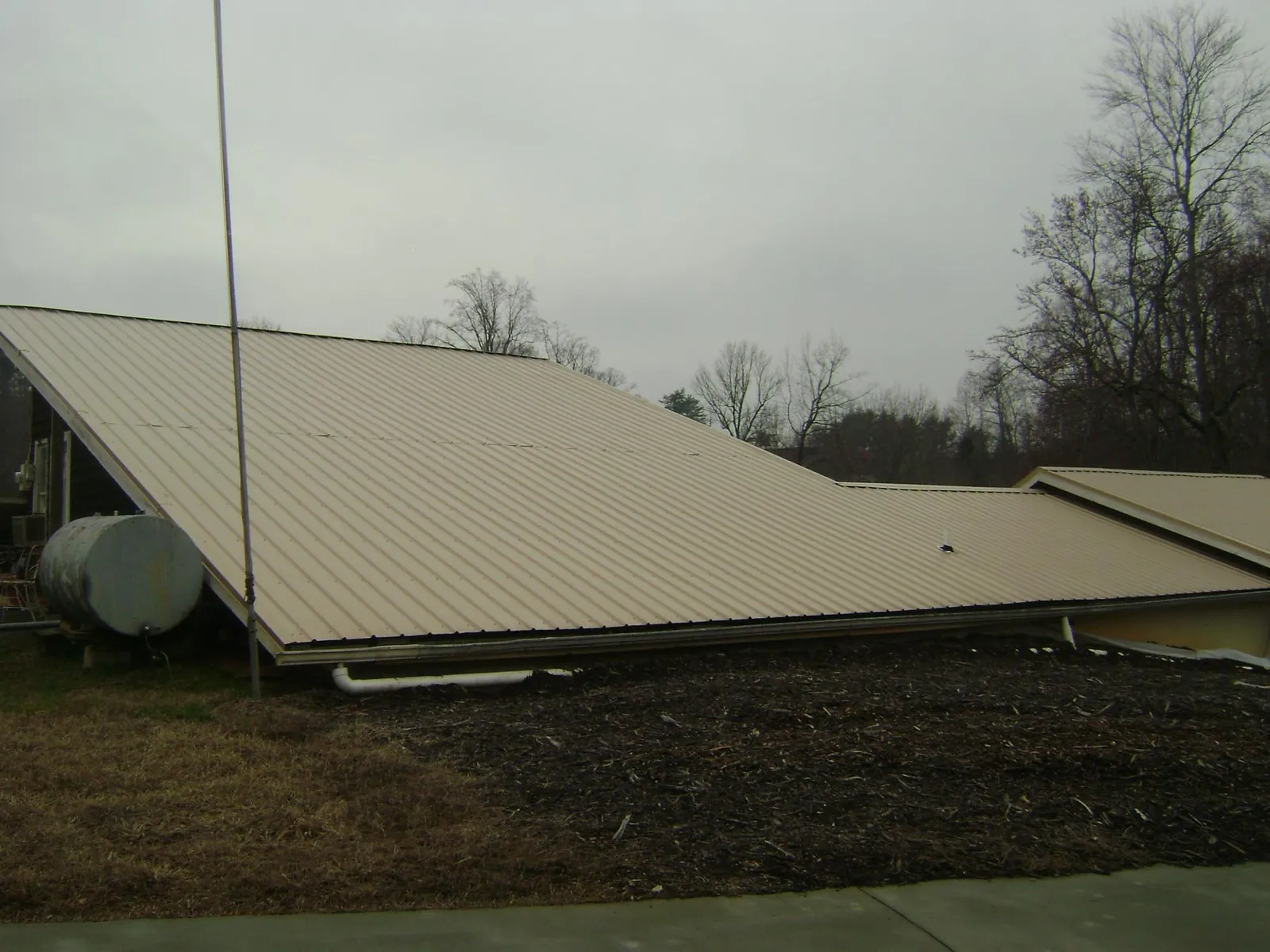 Wide tan metal roof plane seen from the ground beside a propane tank in Glade Park