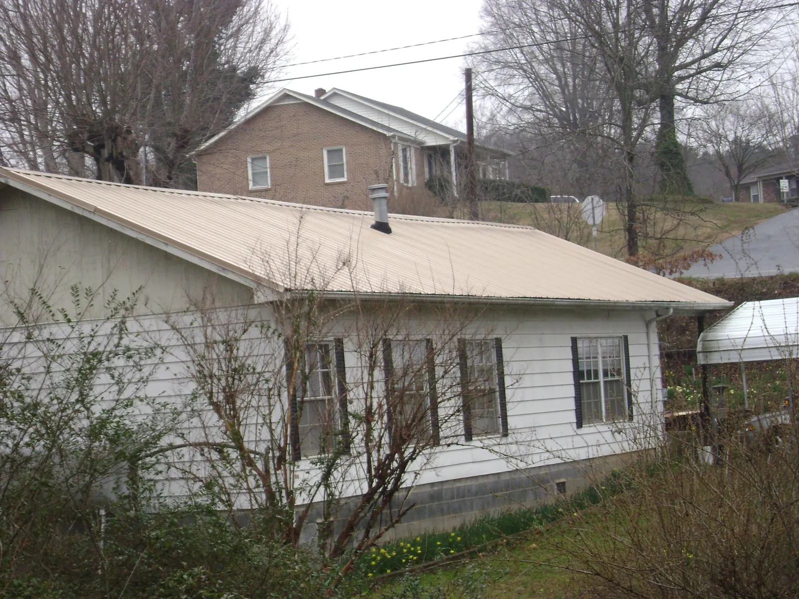 Tan metal roof on a white sided house set into a hillside — Commercial Roofing by Roofing Brothers in Glade Park