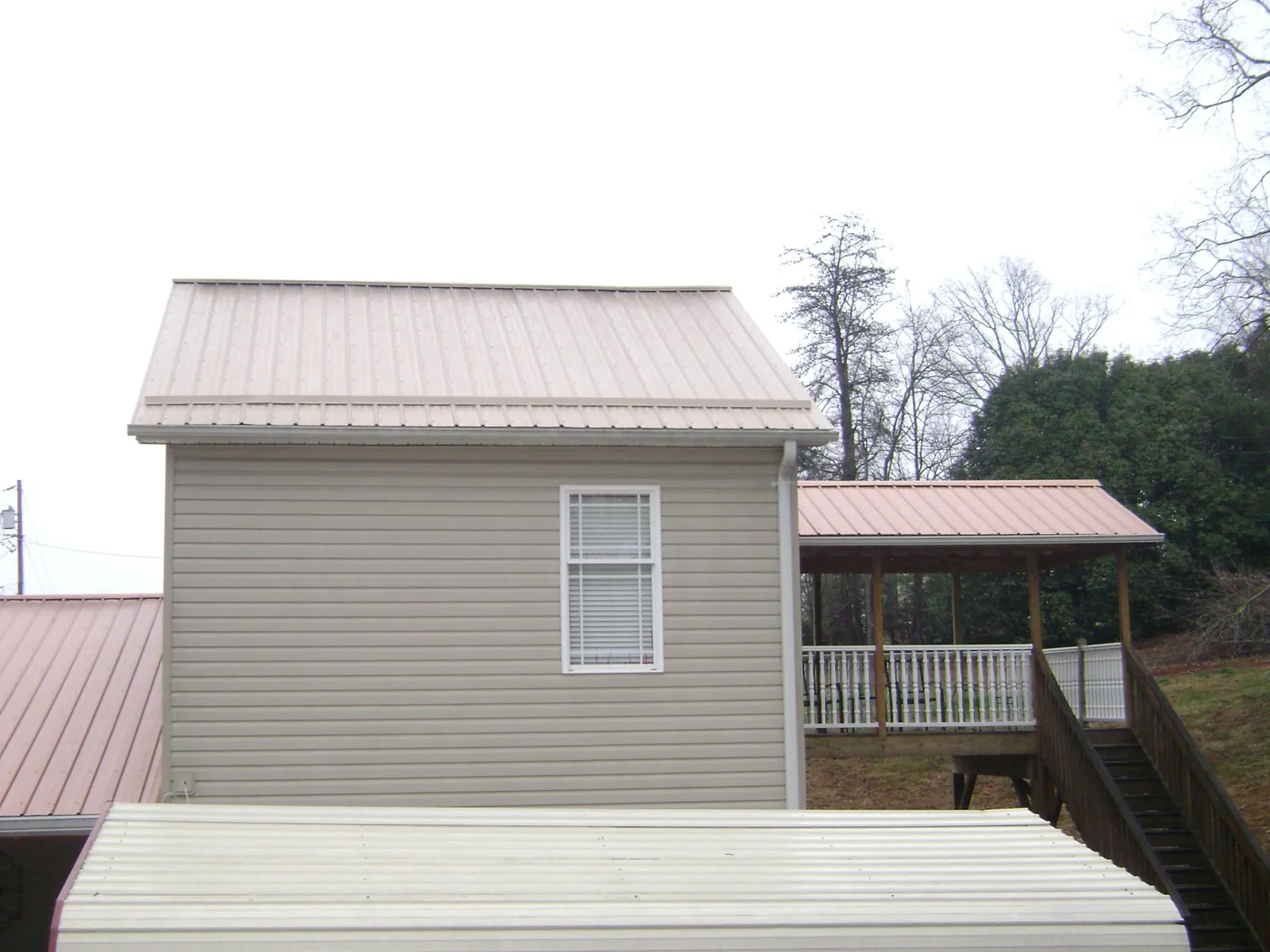 Tan metal roofs on a two story addition and attached porch, from a Roof Replacement job in Glade Park